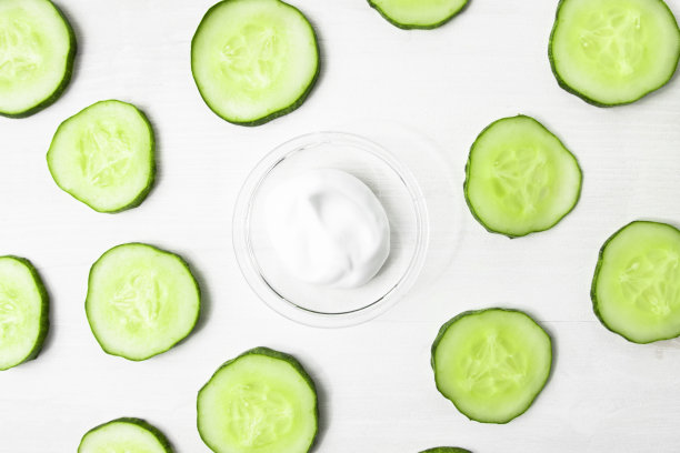 沐浴乳样品和一片片新鲜的绿色黄瓜放在白色的木桌上。一种保湿、滋养身体的疗法图片下载