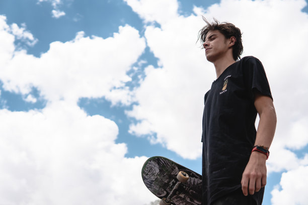 年轻的滑板手以天空为背景，手里拿着滑板图片下载