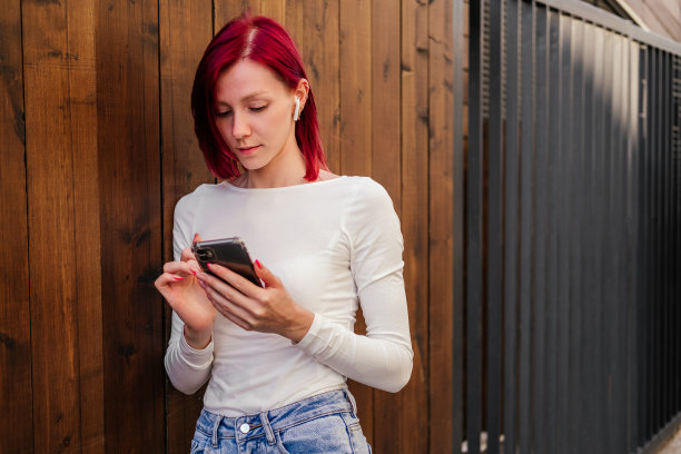 年轻女子戴着耳机，手持智能手机站在户外。在城市里听音乐的女孩图片下载