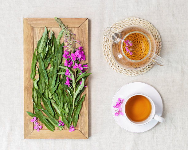 草药茶从kipreya叶在白色杯子亚麻织物桌子背景，杂草绿叶和花在木制托盘。来自野生植物的调味凉茶，疗愈热饮。图片下载