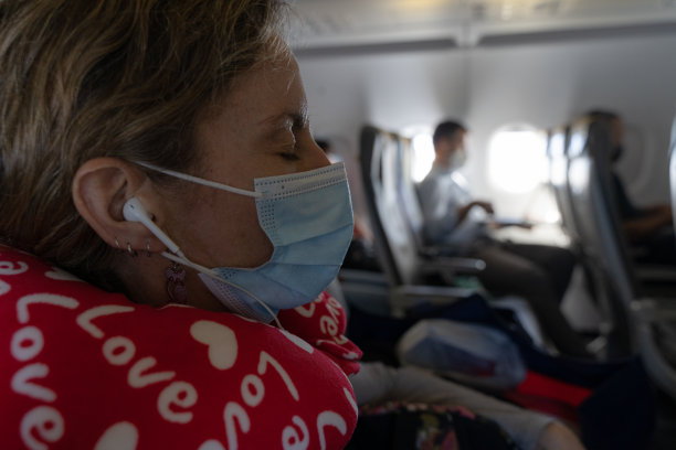 女性在飞机上睡觉时戴口罩、耳机和颈枕图片下载
