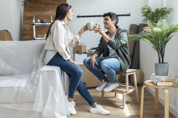 年轻漂亮的夫妇一边喝着咖啡，一边放松地从他们的新房子周围的纸板箱图片下载