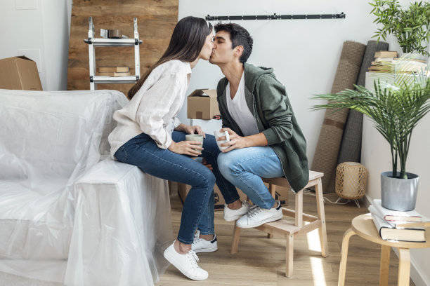 一对美丽的情侣在搬到他们的新房子的纸箱周围放松的时候接吻图片下载