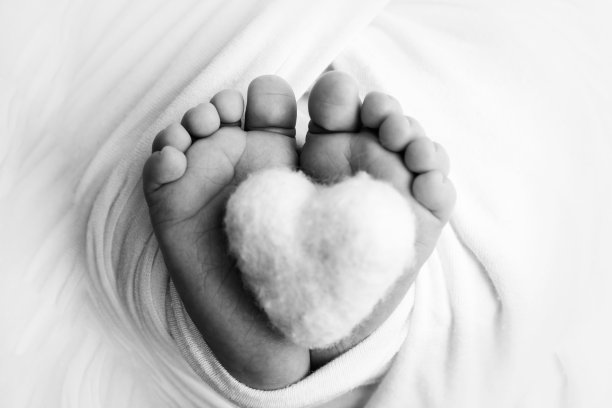 新生婴儿的小脚。婴儿柔软的脚在毯子里。新生儿的脚趾，脚跟和脚的特写。把心编织在婴儿的腿上。微距摄影。黑色和白色。图片下载