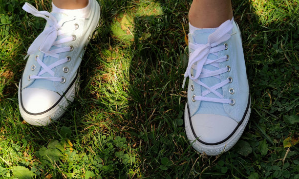 绿草地上穿着白色运动鞋的女孩的腿。靠近一双白色的鞋子在一个女孩的腿上，背景是绿色的草地图片下载