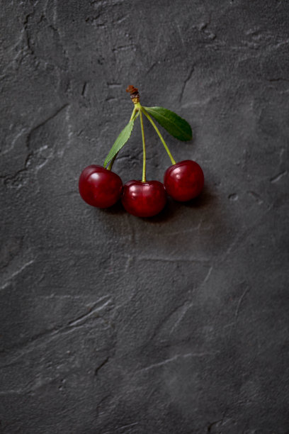 成熟樱桃的红色浆果，绿叶在黑色的工艺背景。浆果的特写照片。图片下载