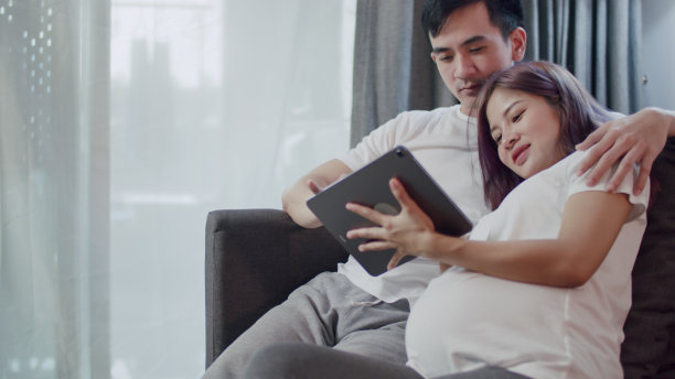 幸福的白人丈夫和怀孕的妻子一起在平板电脑上看她的新生儿的超声波照片，并在家里生活的网上购物。图片下载