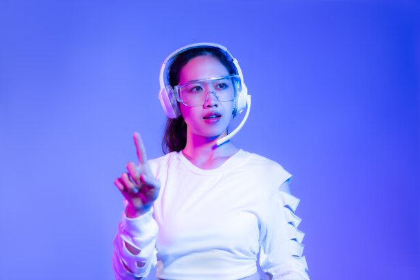 年轻的亚洲女性穿着白色衬衫，戴着耳机，摆姿势说话，手指指着蓝色的背景。图片下载