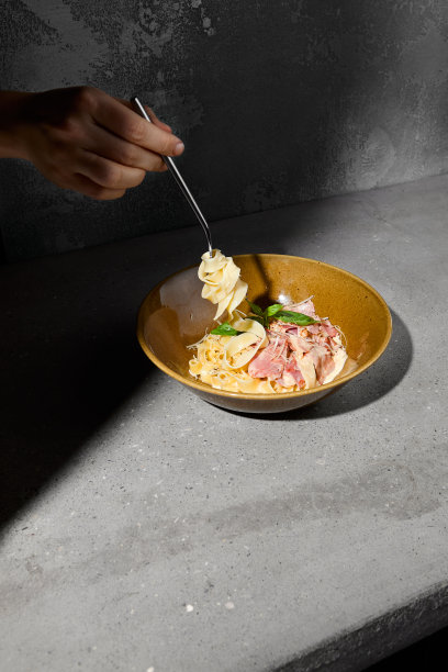 女人用叉子叉着意大利面。烤意大利宽面条在陶瓷板上灰色桌子硬阴影。灰石质背景上有女性手的意大利宽面。图片下载