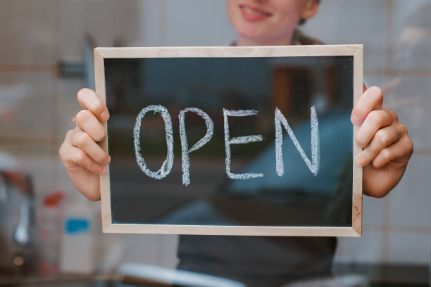 年轻漂亮的女人在一个围裙的咖啡馆工作人员持有一个标志打开反对图片下载