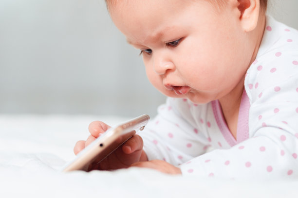 一名白人婴儿躺在床上玩智能手机的特写照片。儿童游戏与现代设备的概念图片下载