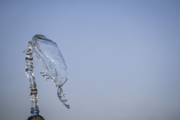 天空背景上的女人手拿着一瓶水。飞溅图片下载