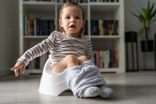 一个一岁的小白种人女婴坐在家里的儿童便盆上，在白天的地板上完整的正面视图拷贝空间图片下载
