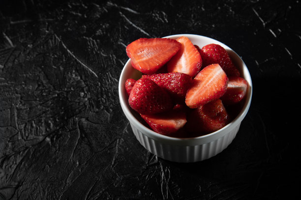 美味的草莓放在黑色背景的碟子里。图片下载