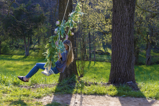 年轻的女士在装饰着鲜花的户外秋千上荡秋千图片下载