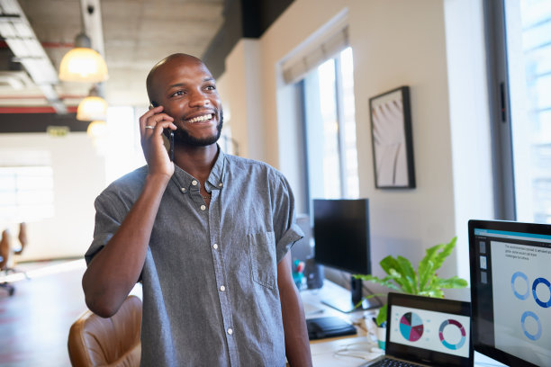 一个黑人商人微笑着站在时髦的办公室里接电话图片下载