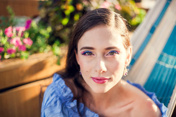 一位浓妆艳抹、一头黑发的年轻美女坐在一家城市咖啡馆夏日露台的吊床上，面带微笑地看着镜头图片下载