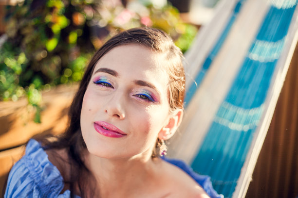 一位浓妆艳抹、一头乌黑长发的年轻美女坐在一家城市咖啡馆夏日露台的吊床上，面带微笑地看着镜头图片下载