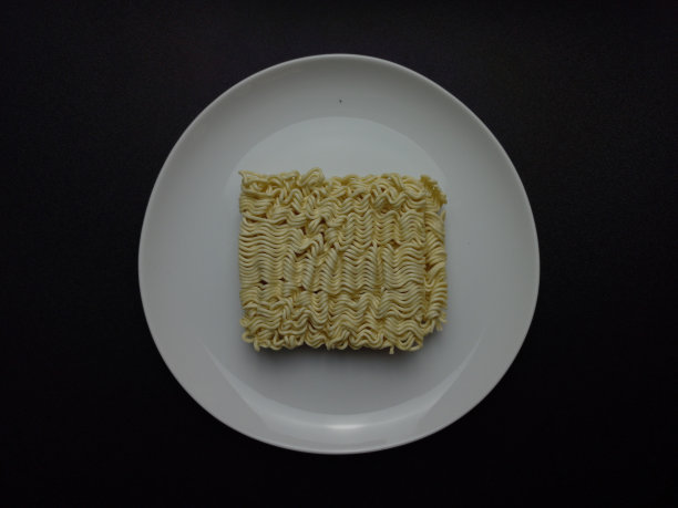 一个生方便面放在一个白色的盘子上，孤立在黑色的背景上。图片下载