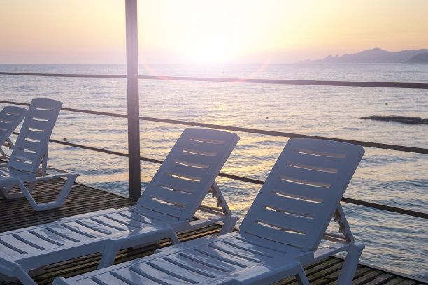 在豪华的热带度假酒店里，许多空荡荡的白色躺椅排成一排。从高码头俯瞰大海和日落。暑假和休假，旅游和旅游的概念。图片下载