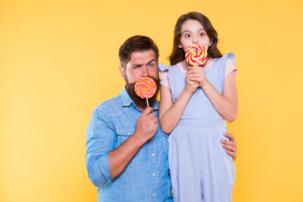 享受美好的一天。父亲和孩子用糖果黄色的背景遮住嘴巴。糖果店。棒棒糖或抽油。含糖的治疗。糖果工厂和糖果。家庭时间。甜蜜的世界图片下载