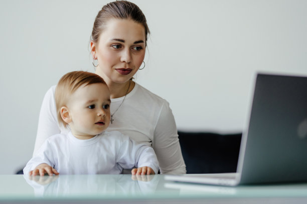 年轻的单身母亲与蹒跚学步的新生儿婴儿的儿子使用笔记本电脑，搜索网络，一起看动画片。休产假在家工作，做自由职业者，找儿童用品图片下载
