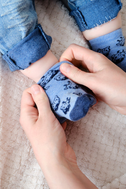 一位母亲给一个脚上的男婴穿了一双蓝袜子。妈妈在床上给一个腿大的孩子穿上衣服。图片下载