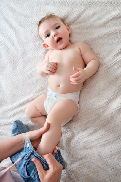 一位母亲给一个小男孩穿上牛仔裤。妈妈给一个快乐的孩子穿上床上的衣服。图片下载