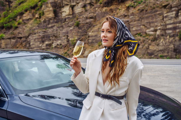 美丽的年轻女子拿着酒杯站在山路上的车旁图片下载