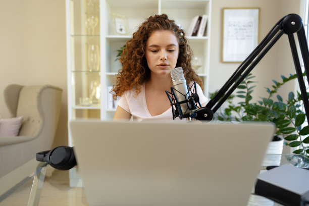 女视频博主看着笔记本电脑，用麦克风录制视频图片下载