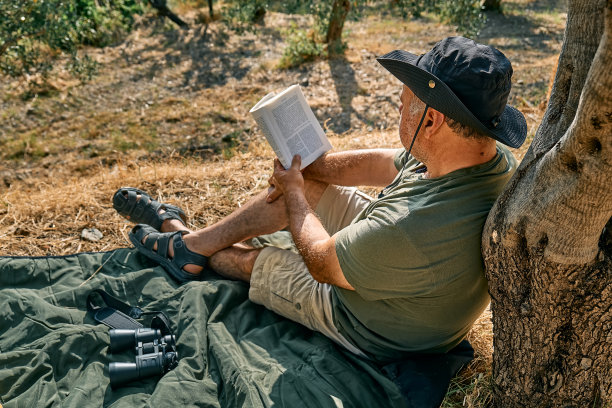 大胡子游客带着书在树下徒步旅行，在阳光明媚的秋天公园里读小说。积极向上的人，健康的生活方式，和谐的理念。幸福和与自然的统一。图片下载
