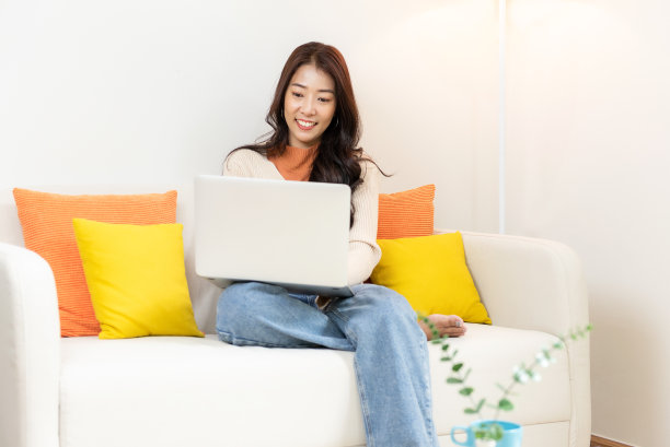 快乐的年轻女子使用笔记本电脑在家里网上购物。生活方式放松和冷静喝咖啡在客厅。生活方式的概念图片下载