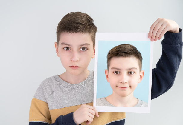 一个表情悲伤的男孩手里拿着一张笑脸的照片。社会的概念图片下载