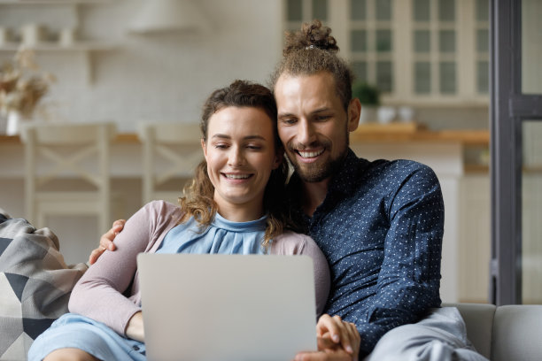 微笑的千禧一代家庭夫妇在家里使用电脑。图片下载