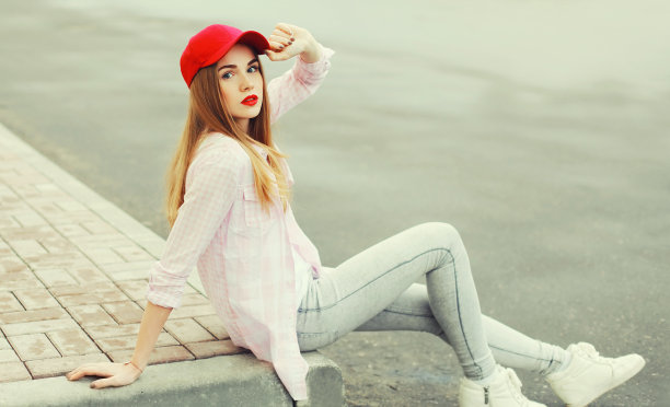 戴着红色棒球帽的金发年轻女子在城市街道上的肖像图片下载