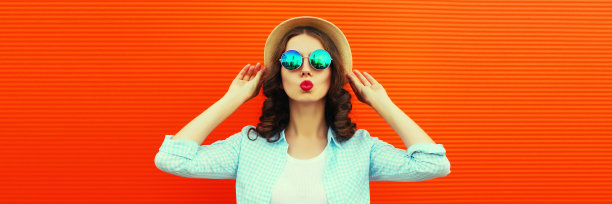 美丽的年轻女子的肖像，她的嘴唇发送甜蜜的空气吻摆戴夏天的草帽在橙色的背景，空白的拷贝空间的广告文字图片下载