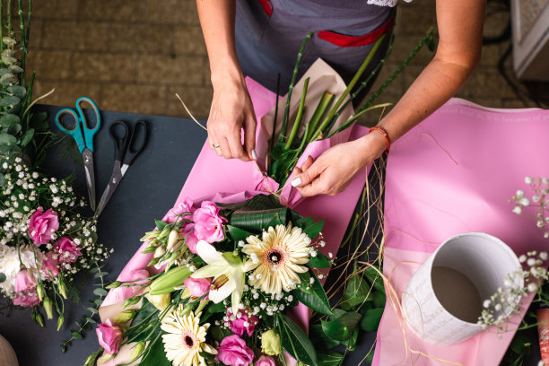 人，园艺和花卉设计概念-从上到下特写的女人或花卉艺术家制作一束花，并在工作室的桌子上系蝴蝶结图片下载