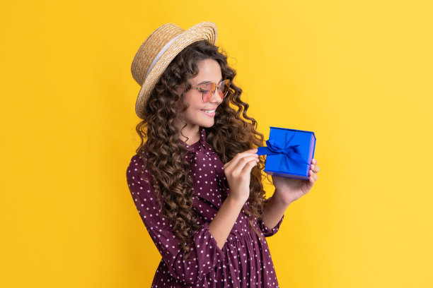 欢快的孩子与卷发握着礼物盒在黄色的背景图片下载