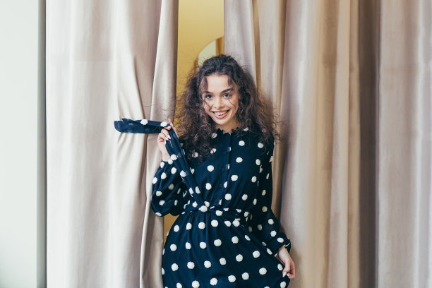 年轻美丽快乐的女人女孩在商场的服装店试衣间里试穿一件黑色的白色圆点的衣服。展示，看镜头，摆姿势，炫耀，想买图片下载