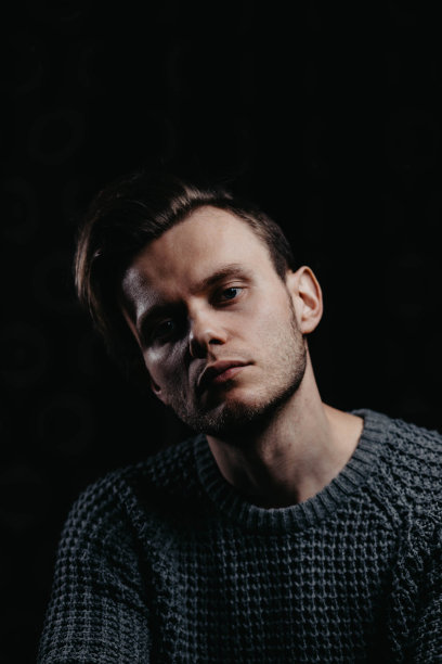 在工作室黑色背景下，一个穿着黑色针织毛衣的英俊年轻人。性感男人肖像。图片下载