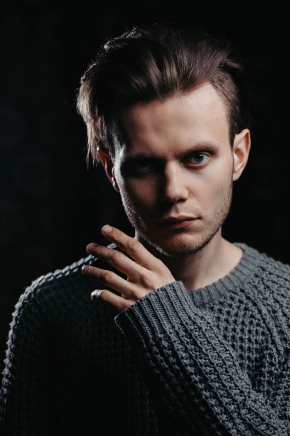 在工作室黑色背景下，一个穿着黑色针织毛衣的英俊年轻人。性感男人肖像。图片下载