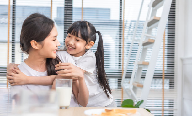 亚洲家庭在客厅享用早餐。小女孩女儿坐在桌子上，和微笑的爸爸妈妈在早上喝牛奶。家庭幸福。图片下载