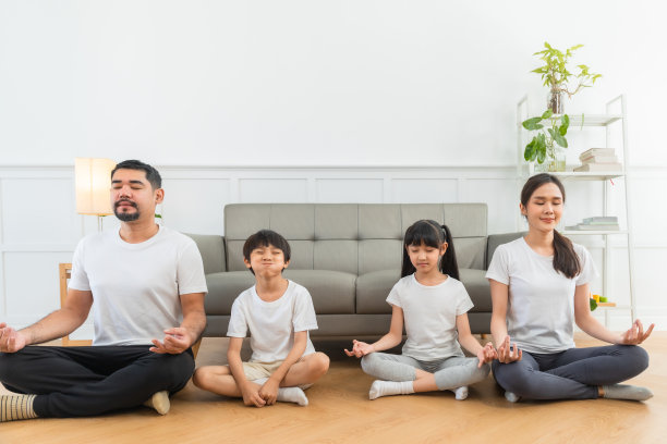 快乐的爸爸妈妈闭着眼睛在地板上冥想莲花的姿势，而兴奋的孩子在沙发上跳跃。图片下载