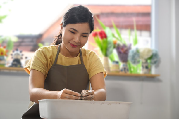 亚洲女陶艺家在创意工作室的陶轮上创作手工陶器。图片下载