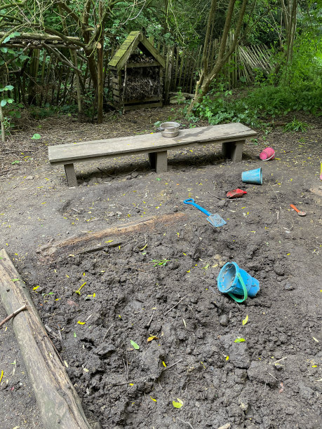 特写图片的孩子们的林地玩耍区域的泥坑和长凳，塑料桶和铲子的泥饼图片下载