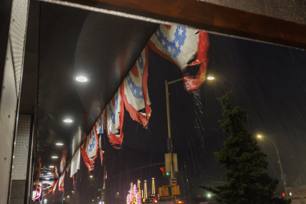 纽约布鲁克林的科尼岛，在倾盆大雨的夜晚，街道上的店面装饰着美国主题的横幅。图片下载