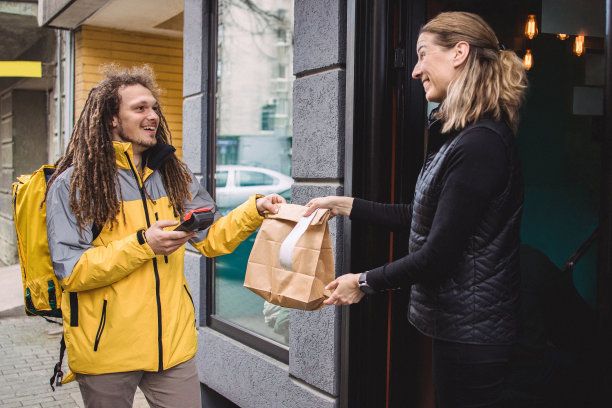 留着脏辫的年轻快递员在餐厅门前拿起一个包裹图片下载