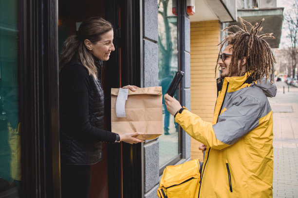 留着脏辫的年轻快递员在餐厅门前拿起一个包裹图片下载