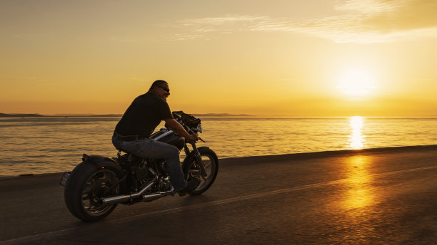 一个男人骑着摩托车在日落的海岸公路上图片下载