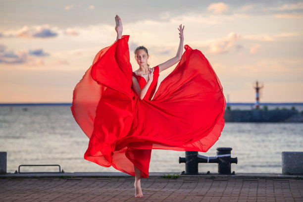 身穿红色飞行裙和紧身裤的芭蕾舞演员，在海堤或海滩上以夕阳的天空为背景图片下载